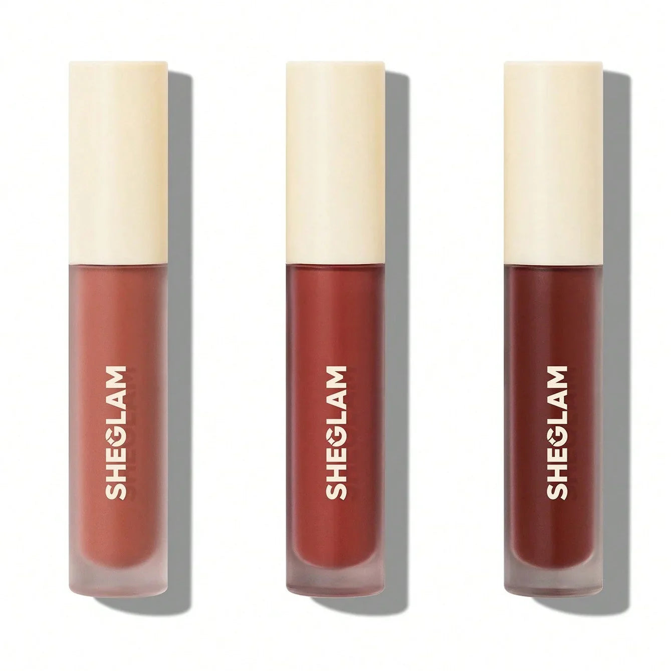 Three SHEGLAM liquid lipsticks in nude, red, and deep burgundy shades with cream caps, perfect for everyday beauty looks.